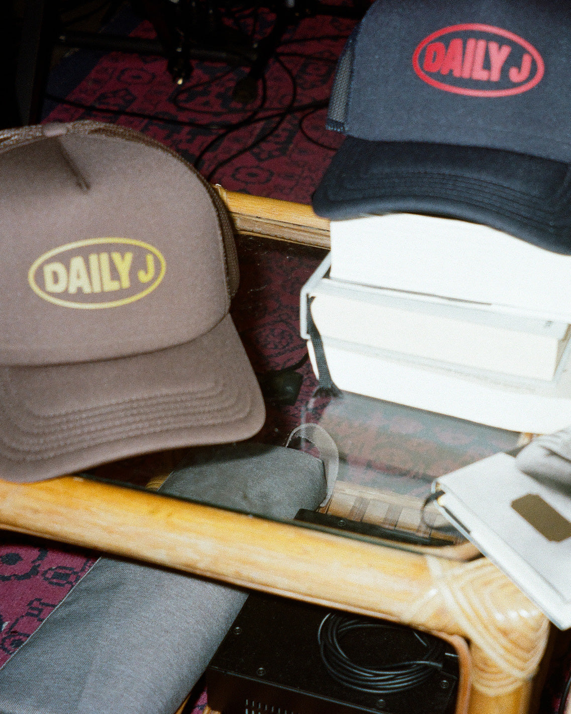 Two hats with 'DAILY J' logo on a table with a newspaper underneath.